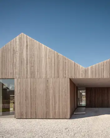 Modern houten huis met schuin dak, grote glazen deur en betonnen voortuin, heldere blauwe lucht als achtergrond