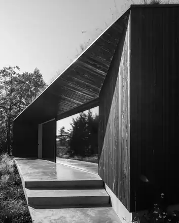 Moderne architectuur met een terras in gepolierd beton, waarbij houten panelen en een overhangend dak de vooraanstaande elementen vormen. 