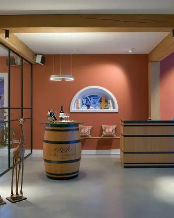 Een modern interieur met een gevlinderde betonvloer, houten balken, een bar met een wijnvat en decoratieve giraffen. 