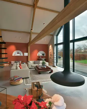 Betonvloer in ruim interieur met houten balken, witte meubels en grote raam met uitzicht op tuin