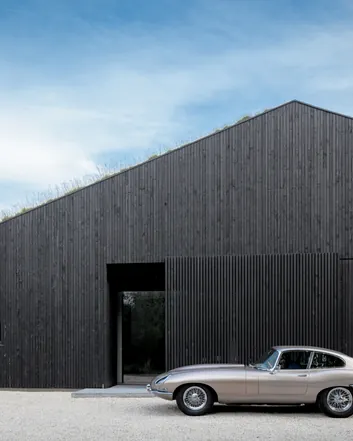 Zwart houten gevel met groen dak, moderne architectuur, betonvloer entree buiten, klassieke auto vooropgesteld